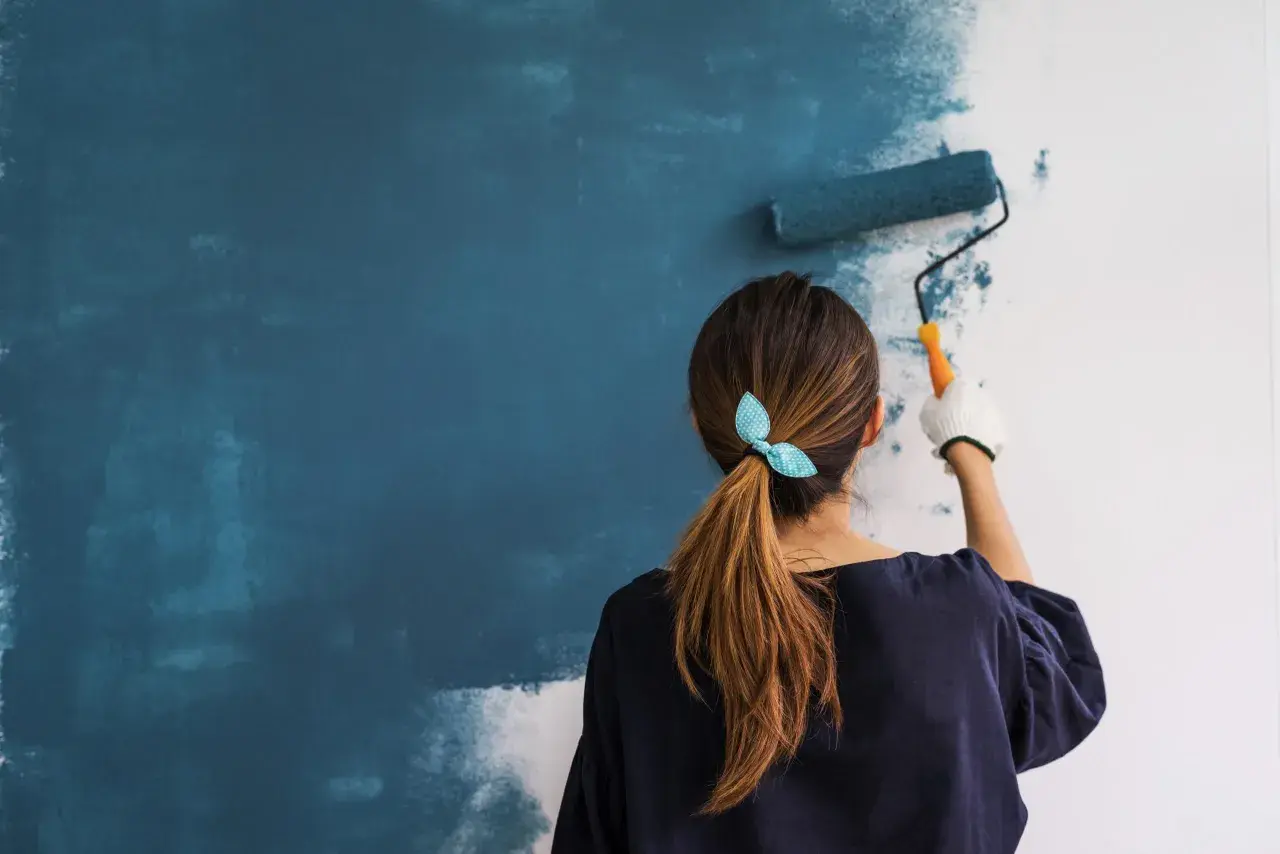 Mujer aplicando imprimación azul en pared con rodillo. Aprende como dar imprimación en paredes para un acabado perfecto.