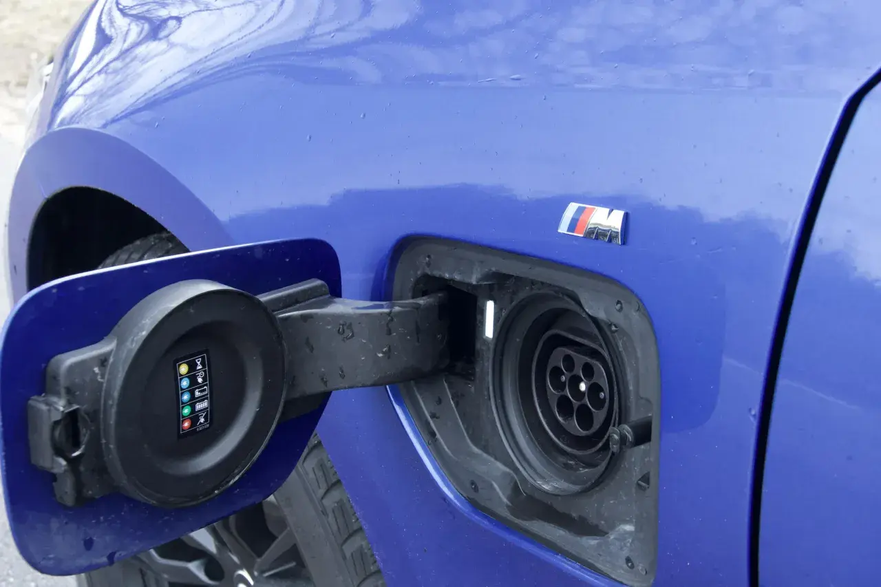 Niebieskie BMW 330e z otwartą klapką gniazda ładowania. Widoczny symbol M.