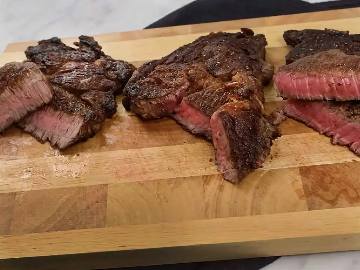 Tre saftiga steak minute-biffar, perfekt stekta med rosa kärna, ligger på en träskärbräda.