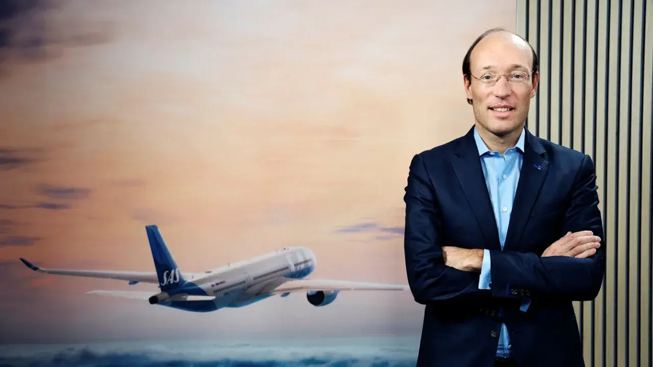 SAS VD, en man i kostym, står framför en bild av ett flygplan i solnedgången.