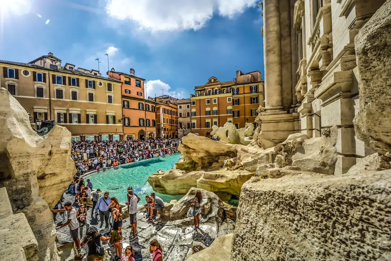 Fontana di Trevi, un vero gioiello tra gli imperdibili di Roma, affollata di turisti che ammirano la sua maestosità sotto un cielo azzurro.