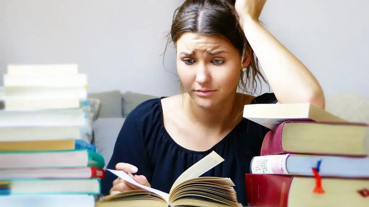 Joven con libros apilados, pensativa, buscando qué hacer cuando te aburres.