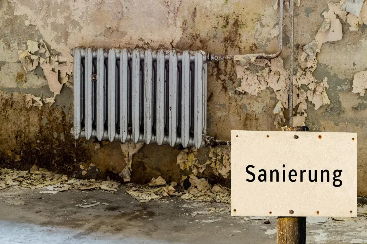 Altes Heizkörper, Wand bröckelt, ein Schild mit "Sanierung" weist auf den Zustand hin. Es ist offensichtlich, dass hier etwas leck und undicht ist.