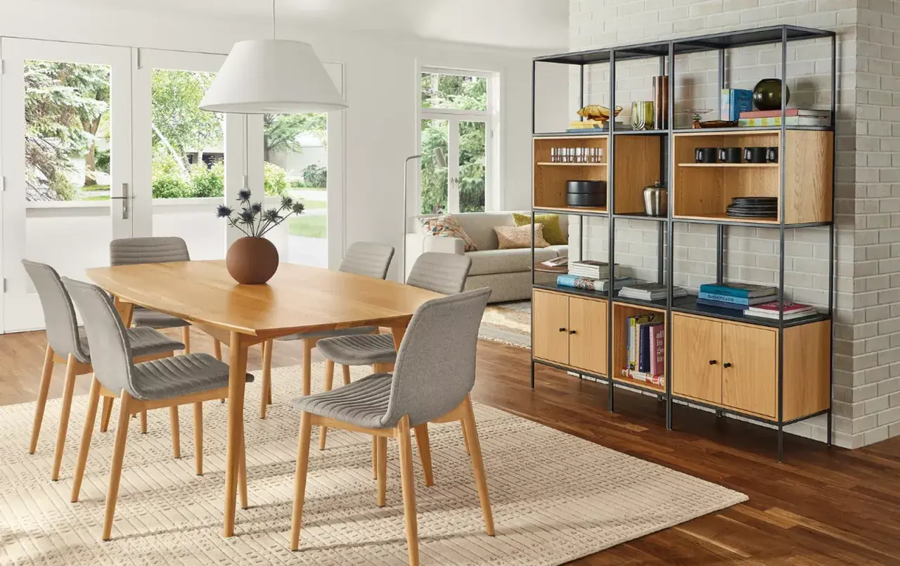 Open living and dining room ideas: a light wood table with grey chairs, a modern shelving unit, and a sofa visible through French doors.