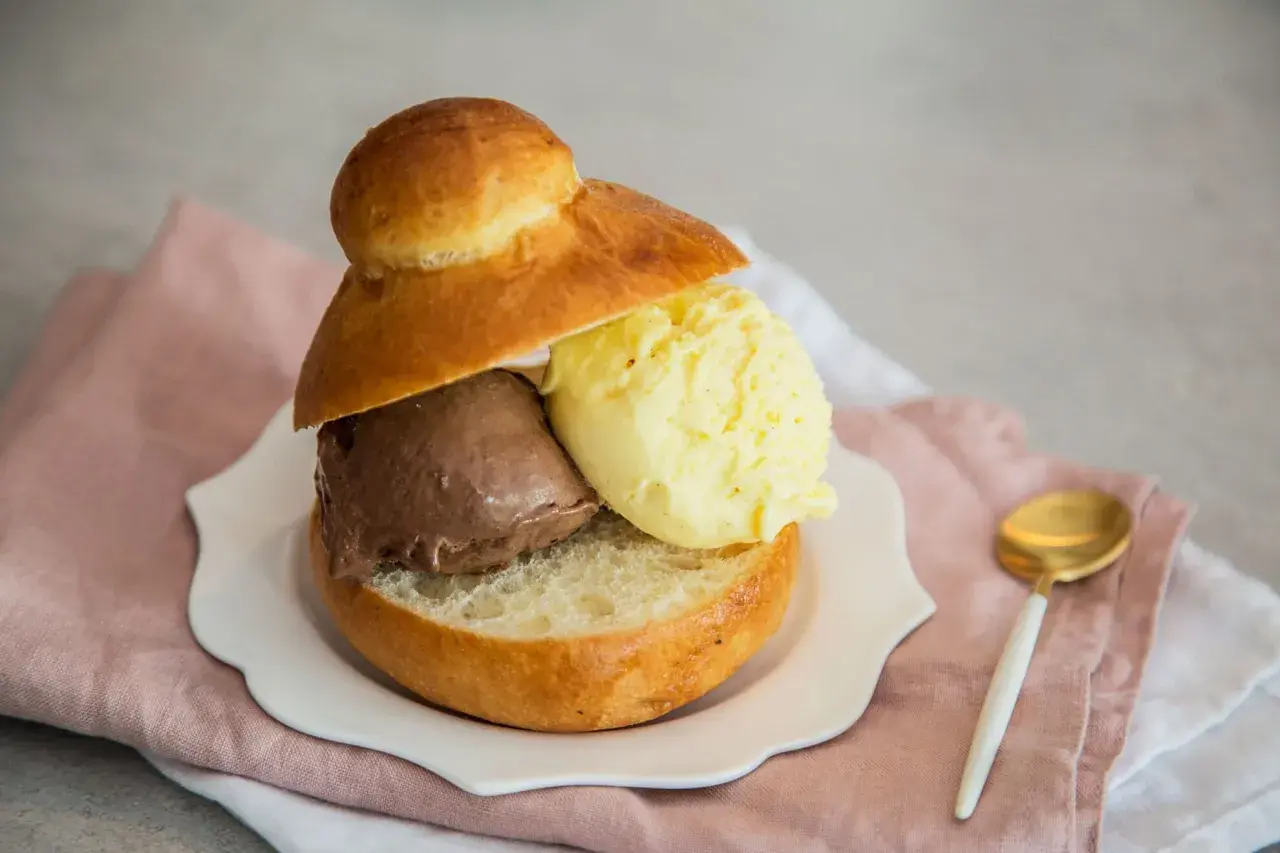 Pyszne lody w bułce: czekoladowe i waniliowe, podane na talerzyku z różową serwetką.