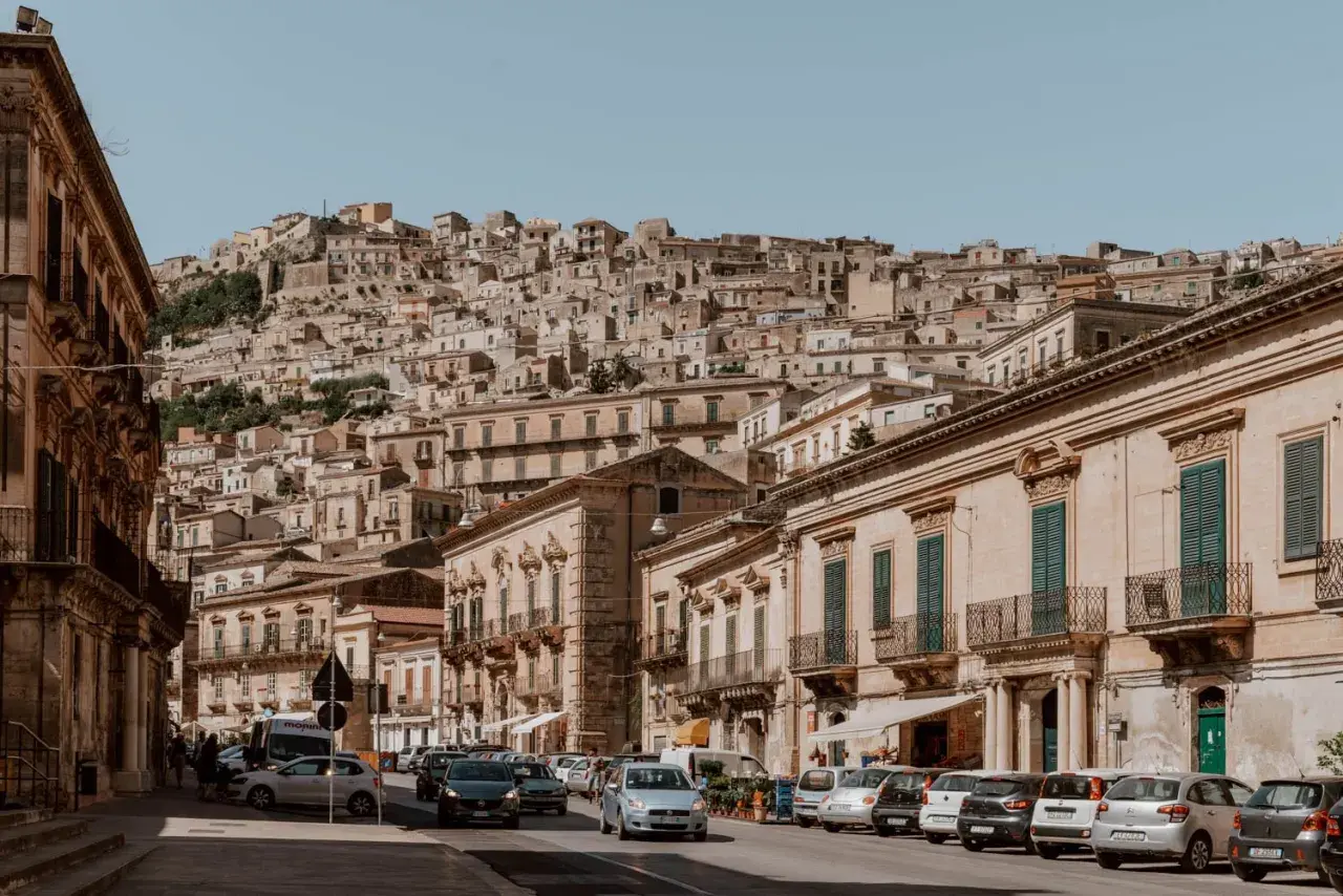 Cars navigate a steep, narrow street in a Sicilian town. Driving here might be challenging, but the views are worth it!