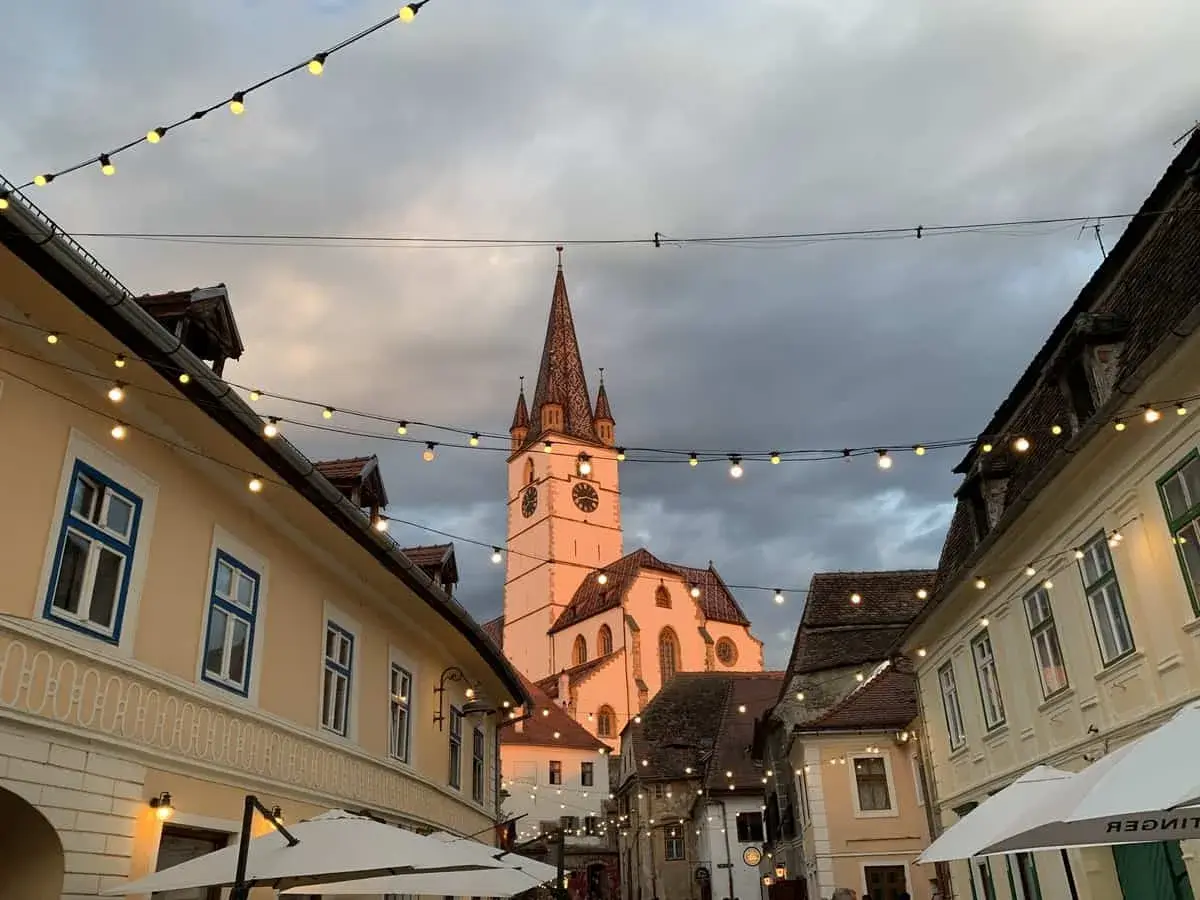 En charmig europeisk stad med en kyrktorn i bakgrunden, kantad av hus och ljusslingor. Perfekt för en resa till billigaste landet i Europa.
