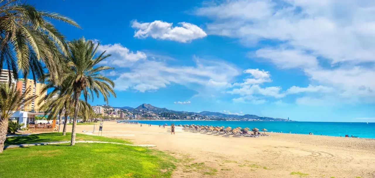 Malaga w maju: słoneczna plaża z palmami, turkusowe morze i góry w tle. Idealna pogoda na wypoczynek.