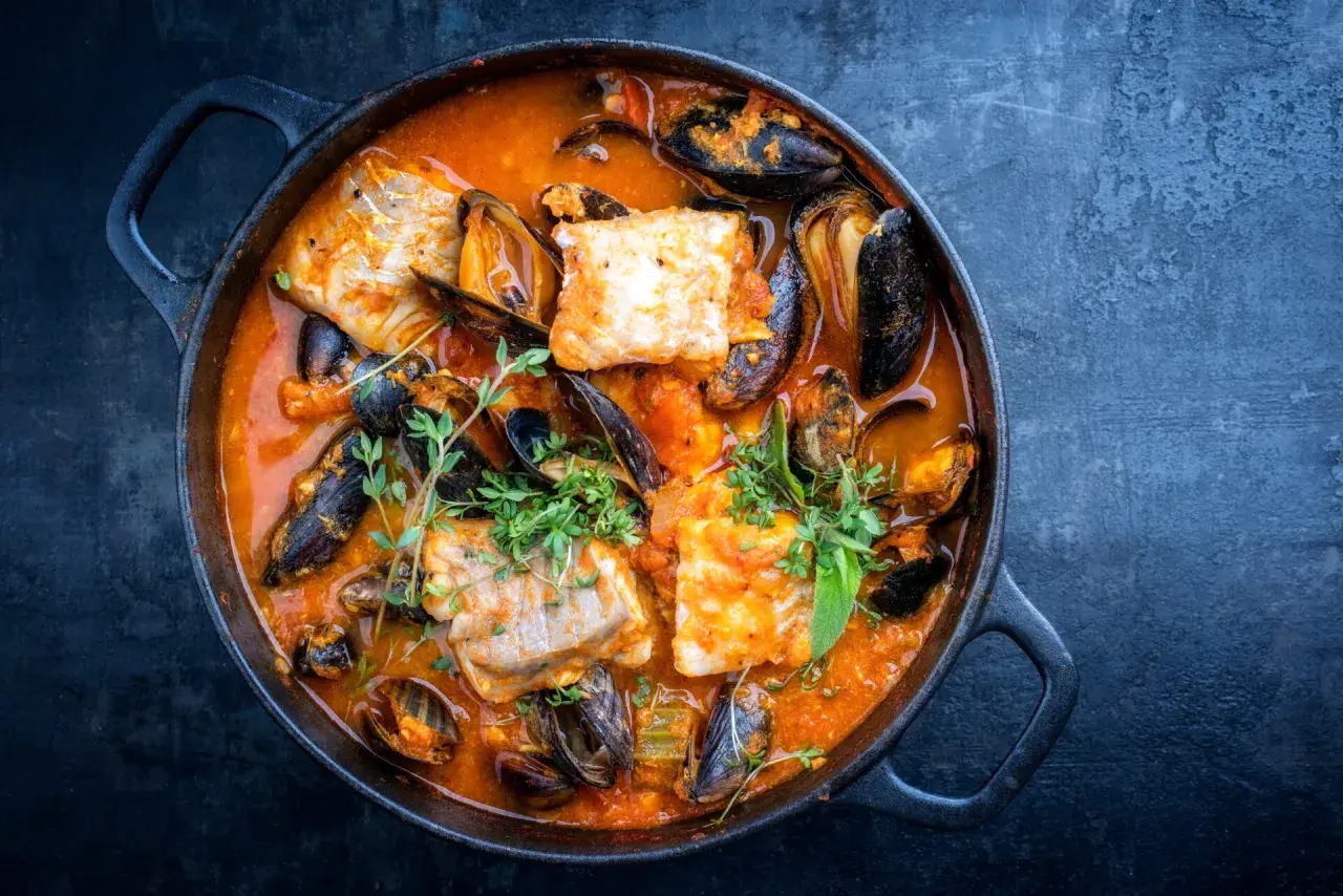 Una ricca zuppa di pesce in una pentola di ghisa, con pezzi di pesce bianco, cozze e erbe aromatiche fresche.
