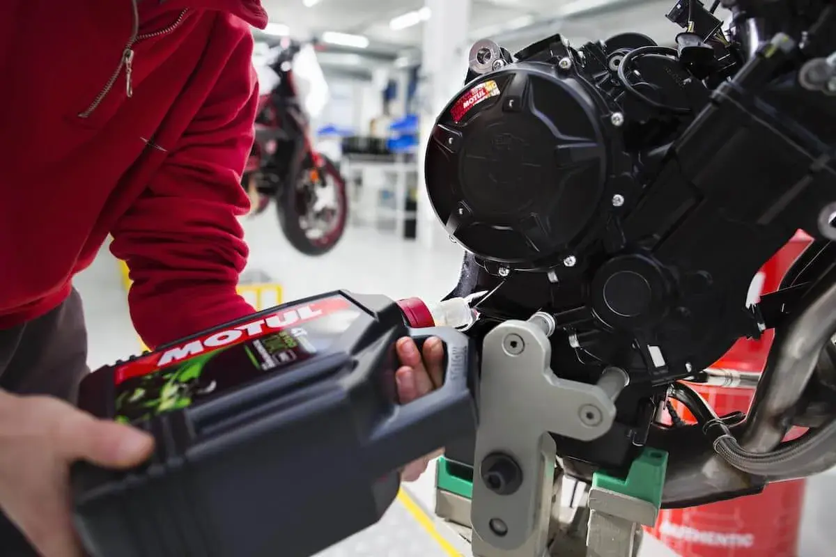 Osoba w czerwonej bluzie nalewa olej Motul do silnika motocykla. Pamiętaj, co ile wymieniać olej w motocyklu, by zapewnić mu długą żywotność.