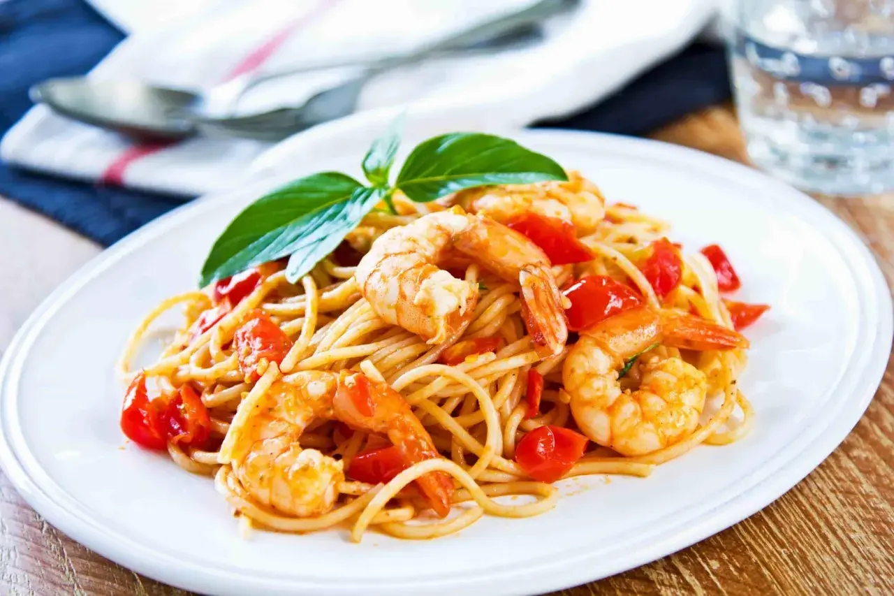 Un piatto invitante di pasta con gamberetti e pomodorini, guarnito con basilico fresco.