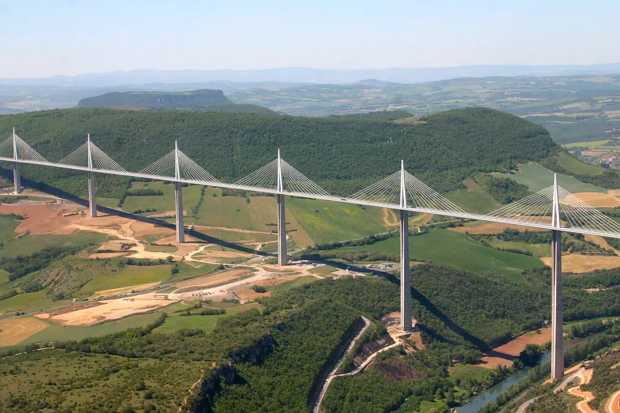 Najwyższy most w Europie, Viadukt Millau, przecina zieloną dolinę z imponującymi pylonami i stalowymi linami.