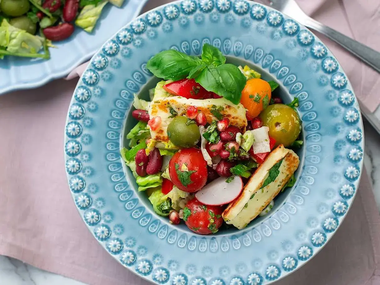 En färgstark sallad med grillad halloumi, tomater, oliver, bönor och granatäpple. Ett perfekt sallad recept för en lätt lunch.