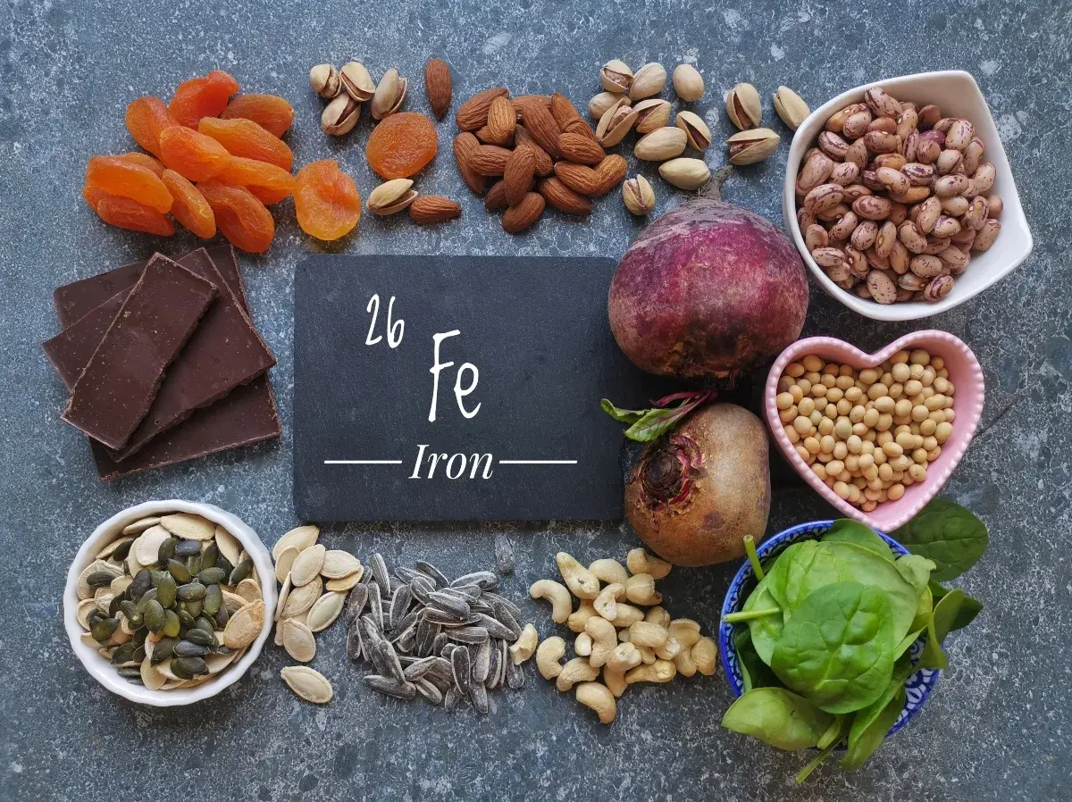 Una tavola ricca di alimenti ricchi di ferro: cioccolato fondente, albicocche, mandorle, pistacchi, barbabietole, fagioli, soia, spinaci, semi di zucca e girasole.