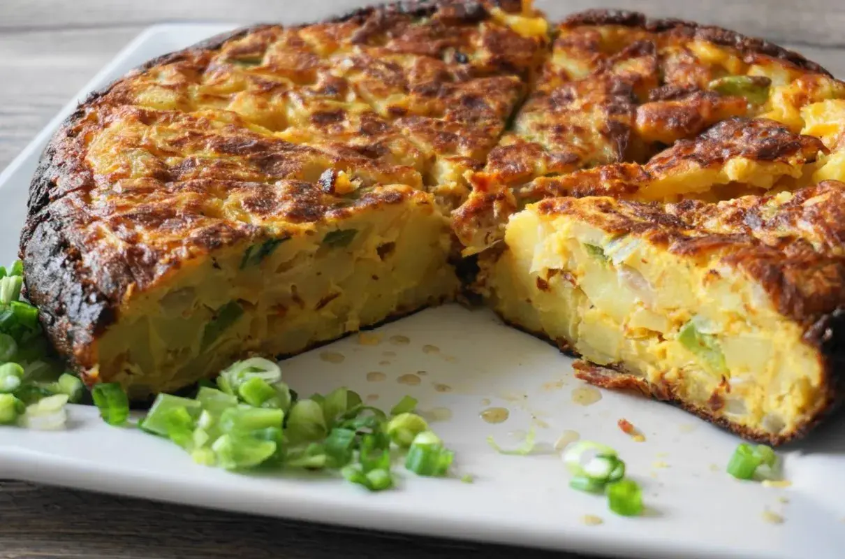 Pyszna tortilla de patatas, pokrojona na kawałki, z zieloną cebulką na talerzu.