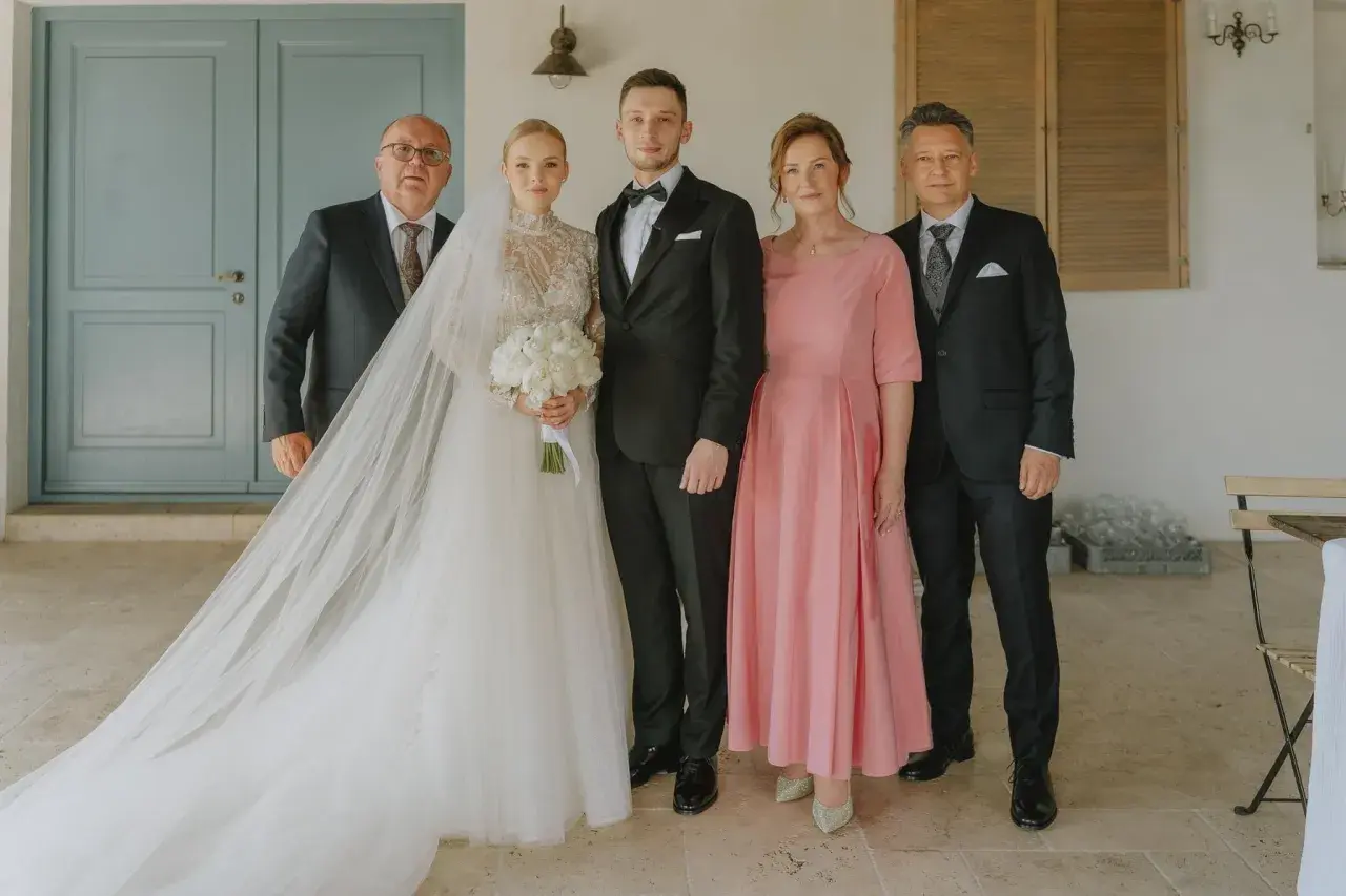 Para weselna z rodzicami. Panna młoda w sukni z welonem, pan młody w garniturze. Obok nich mama weselna w różowej sukience i ojcowie.