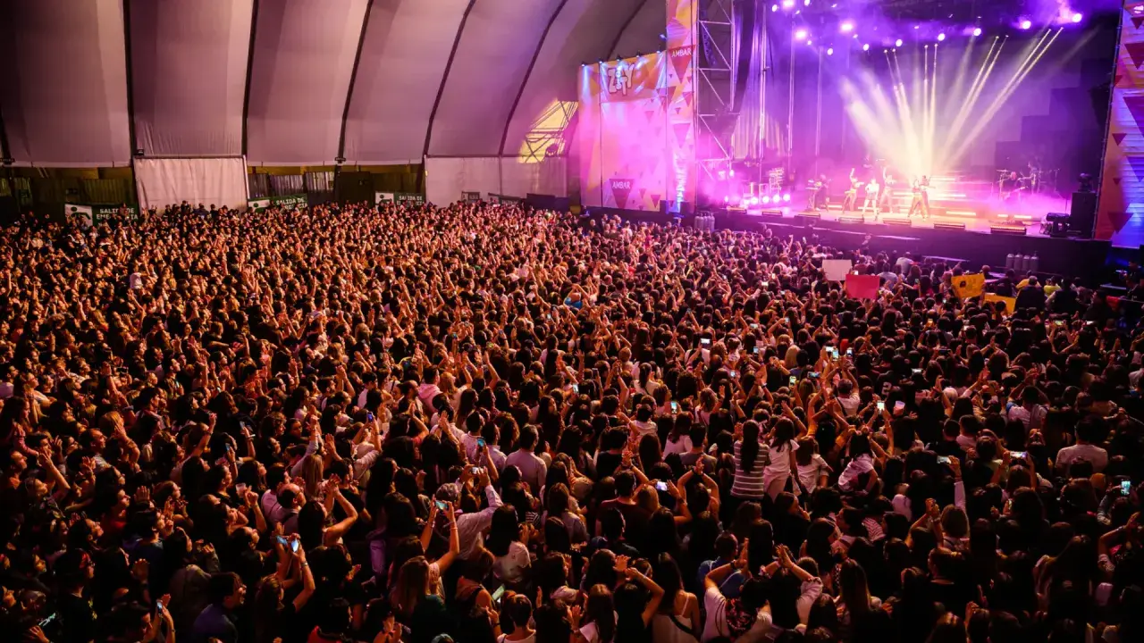 Multitud vibrante en concierto, con luces de escenario y carteles. Se aprecia la **autorización menores espacio Zity** en un cartel.