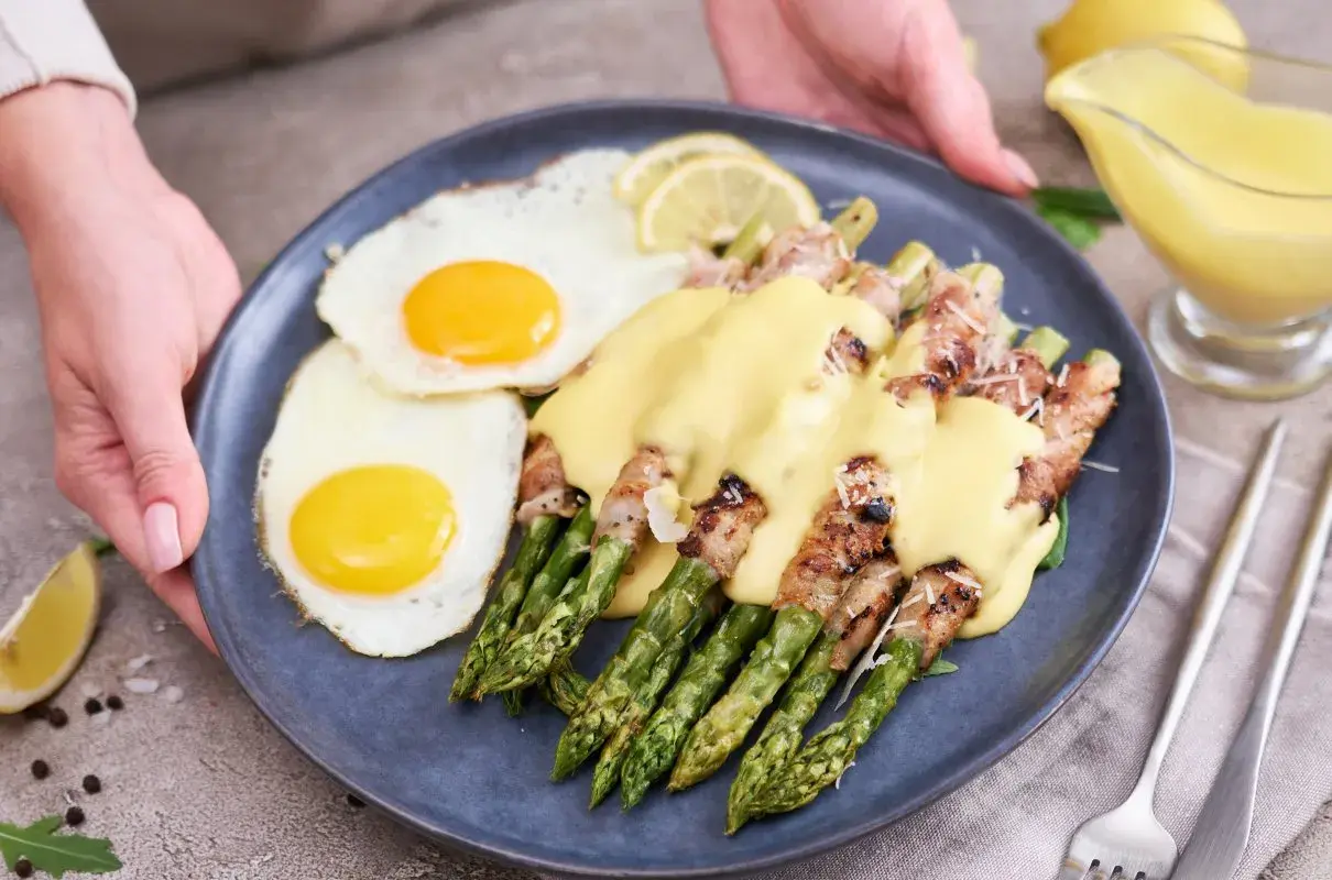 Pyszne szparagi z boczkiem i jajkiem sadzonym, polane sosem. Idealne śniadanie lub brunch.
