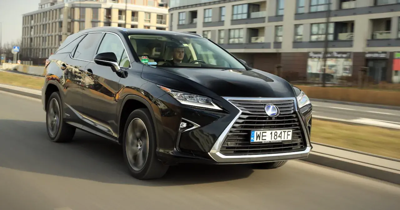 Czarny Lexus RX 450h jedzie ulicą w mieście, za nim widać nowoczesne budynki.