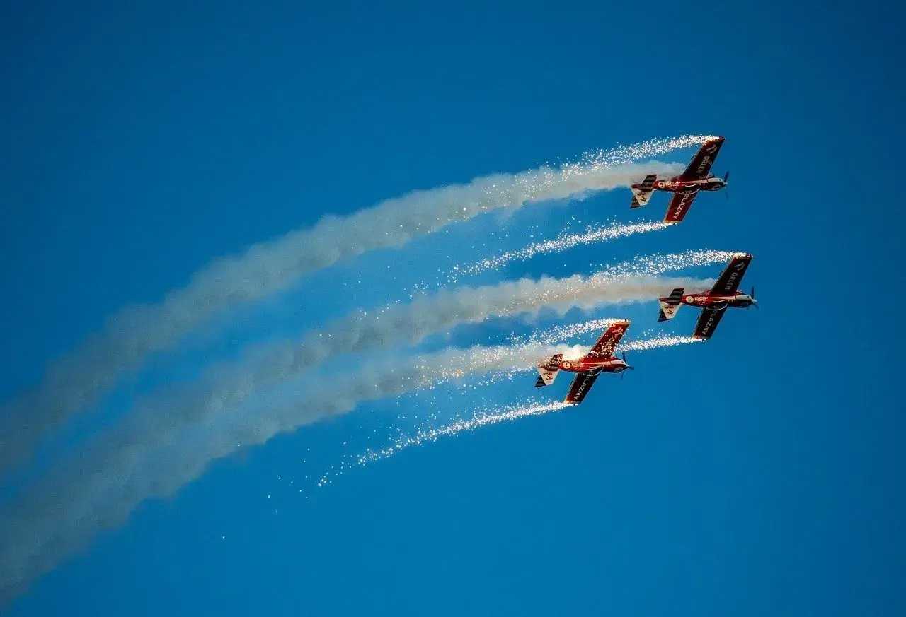 Trzy samoloty akrobacyjne w formacji, wypuszczające dym i iskry na błękitnym niebie. Niezapomniane wrażenia z kiedy air show w Radomiu.