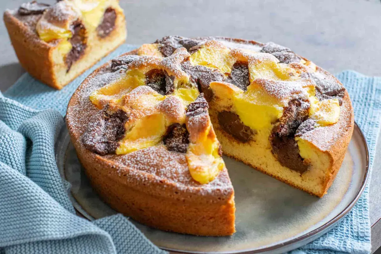 Torta nua con crema pasticcera e cacao, spolverata di zucchero a velo. Una fetta è già stata tagliata, rivelando il morbido interno.