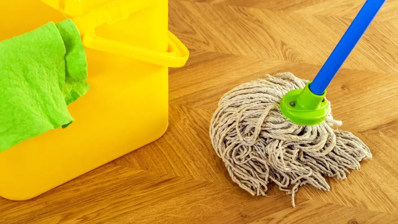 Cubo amarillo con paño verde y una mopa o fregona lista para limpiar el suelo de madera.