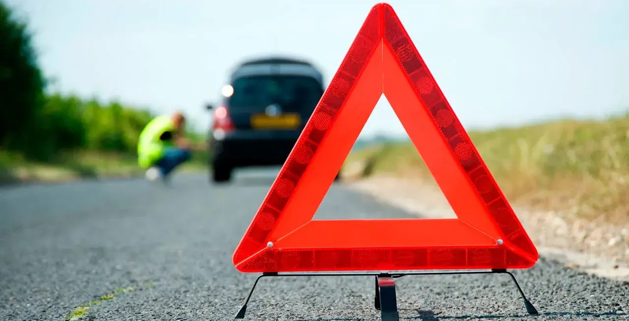 Triángulo de señalización de emergencia en carretera. Un coche averiado y una persona con chaleco reflectante en el fondo. Esquema pas.