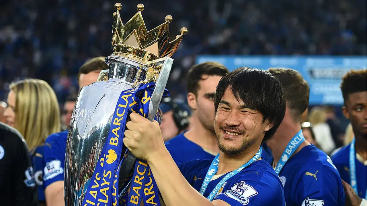 Shinji Okazaki z pucharem Premier League, uśmiechnięty, świętuje zwycięstwo.