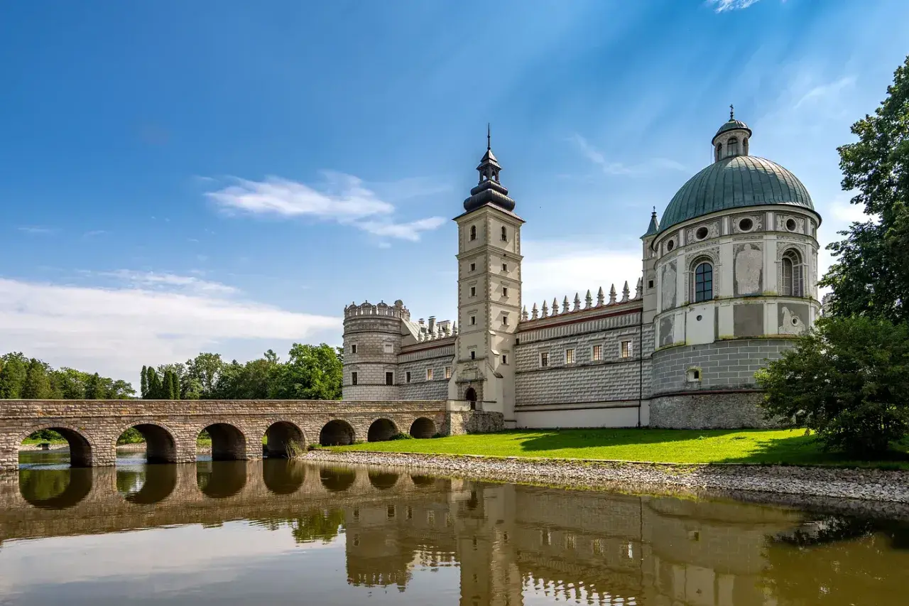 Zamek w Krasiczynie, majestatyczna budowla z wieżą i kopułą, odbija się w spokojnej tafli wody.