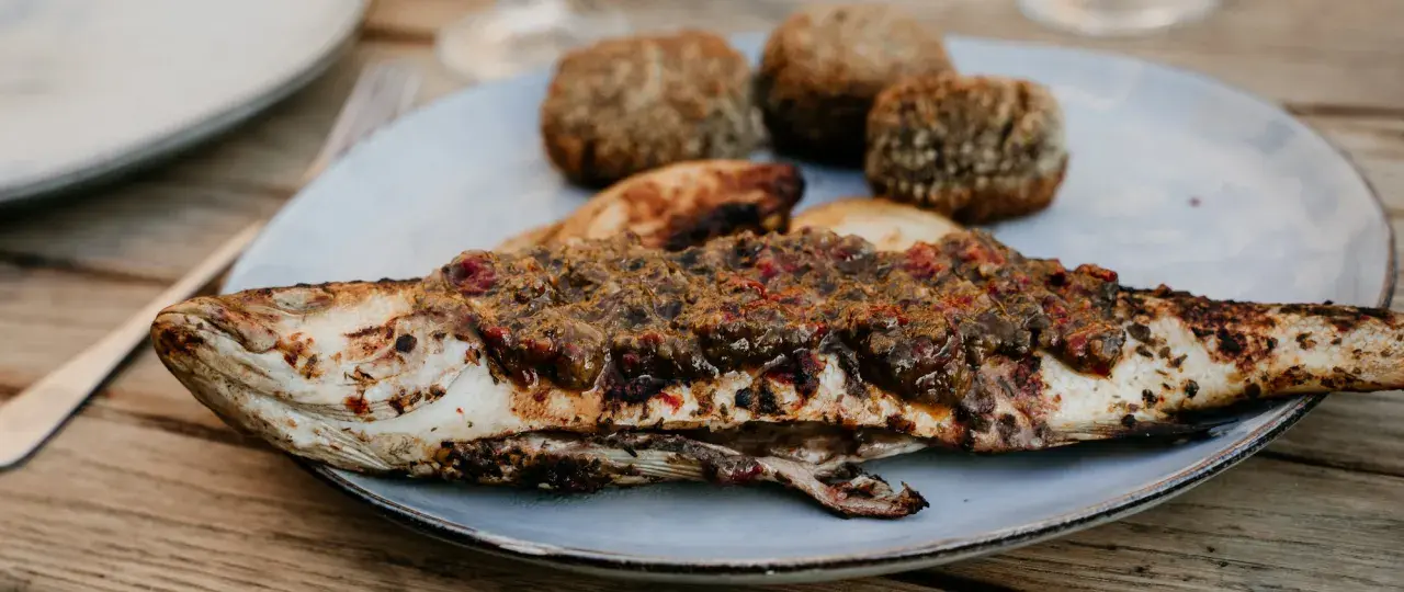 Un loup au barbecue, savamment garni d'une sauce aux herbes et tomates, accompagné de petites boules de pain croustillantes.