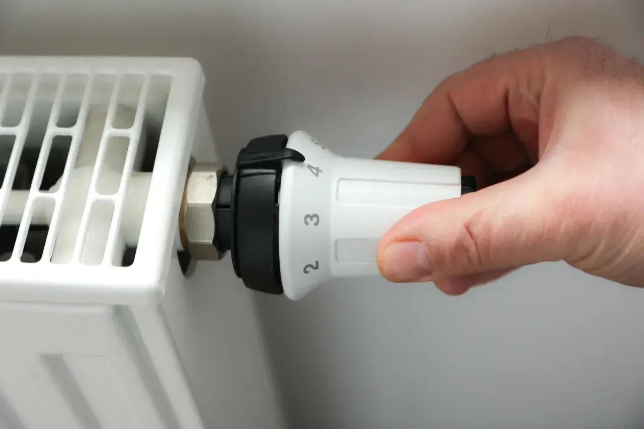 Dłoń reguluje termostat białego grzejnika elektrycznego panelowego, ustawiając temperaturę na 3.