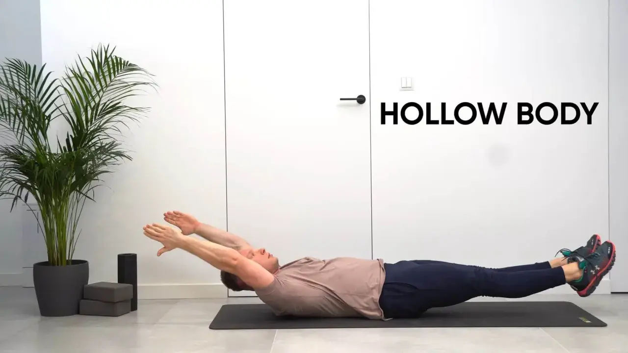 Mężczyzna leży na macie, wykonując ćwiczenie hollow body. Ręce wyciągnięte nad głowę, nogi uniesione.