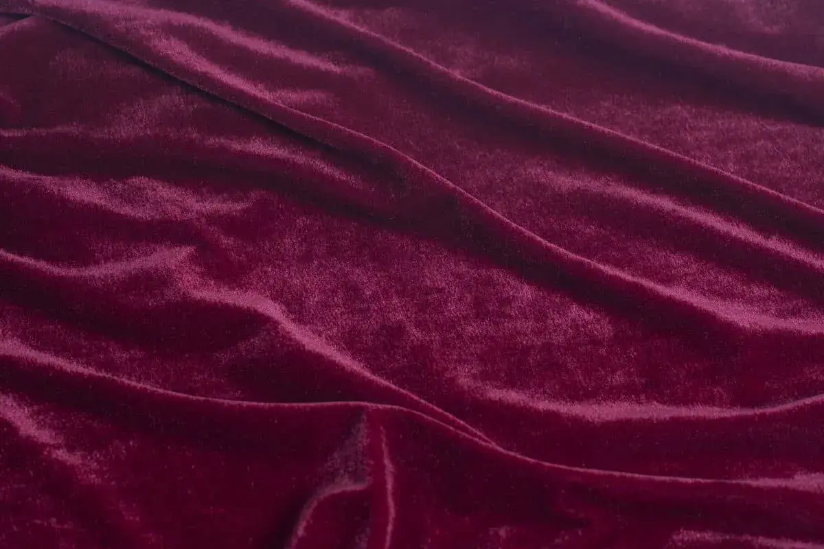 Głęboki, burgundowy materiał o miękkiej, połyskującej powierzchni, podobny do aksamitu, tworzy eleganckie fałdy.