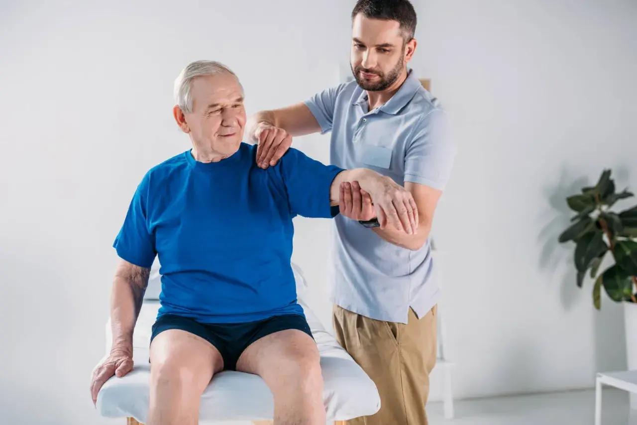 Fisioterapista assiste un anziano con debolezza muscolare, valutando la mobilità del braccio.