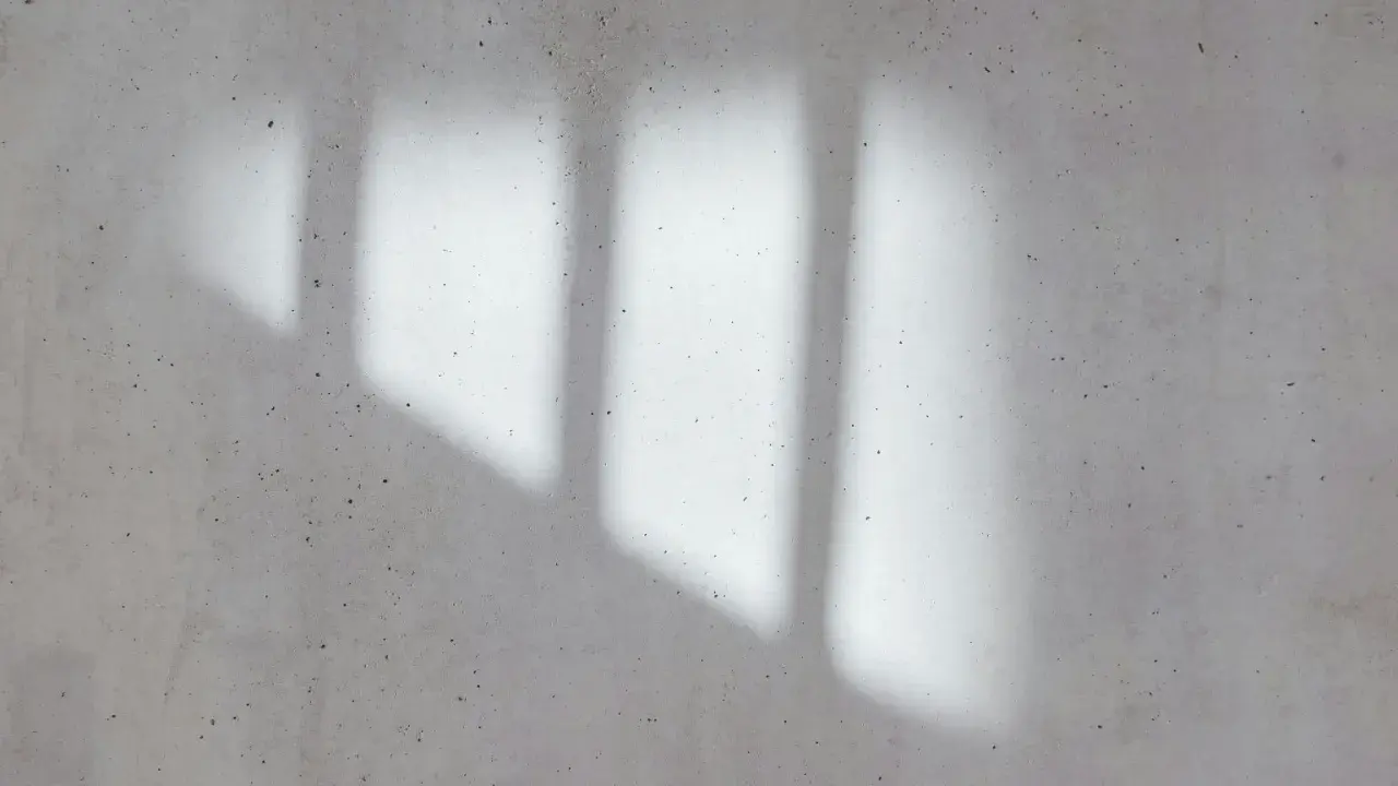 Cień okna pada na betonową ścianę. Ta strumienica fotografia oddaje grę światła i cienia.