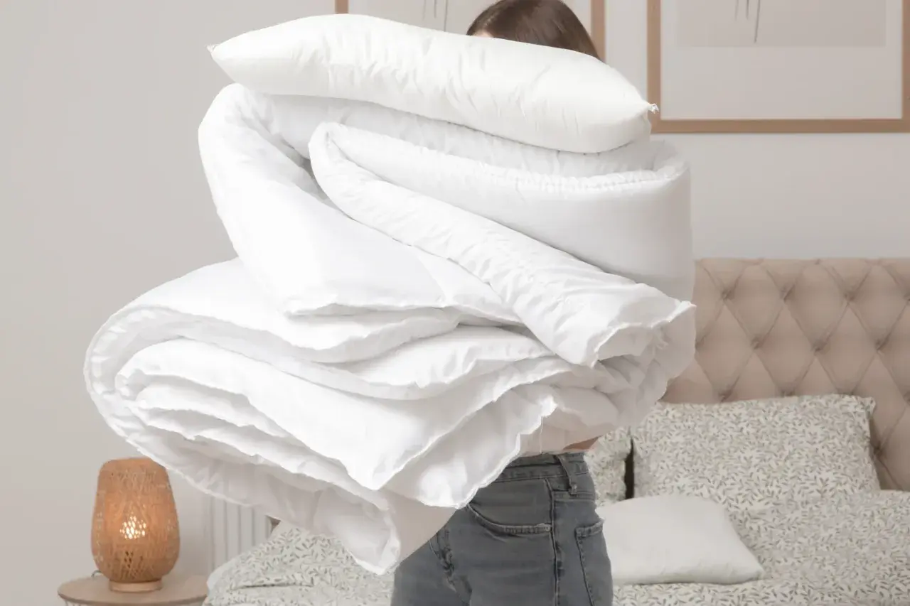 Donna con un grande piumone bianco, pronto per lavare copriletto in lavatrice. La biancheria da letto è piegata in modo ordinato.