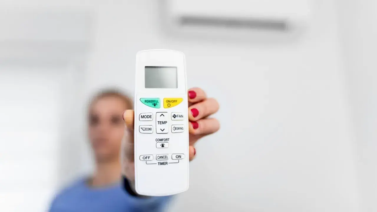 Mano sostiene control remoto de aire acondicionado, listo para activar el símbolo del frío y disfrutar de un ambiente fresco.