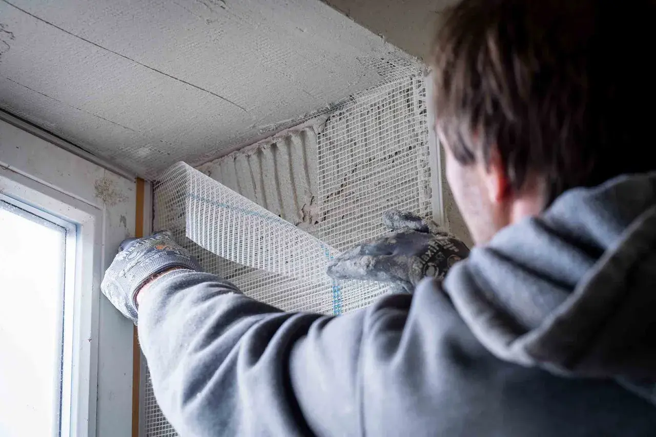 Hand mit Handschuh verputzt Fensterlaibung mit Armierungsgewebe.