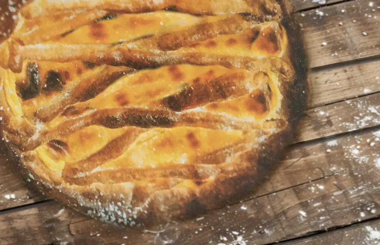 Une tarte au libouli dorée, aux croisillons de pâte bien cuits, repose sur un fond de bois rustique saupoudré de farine.