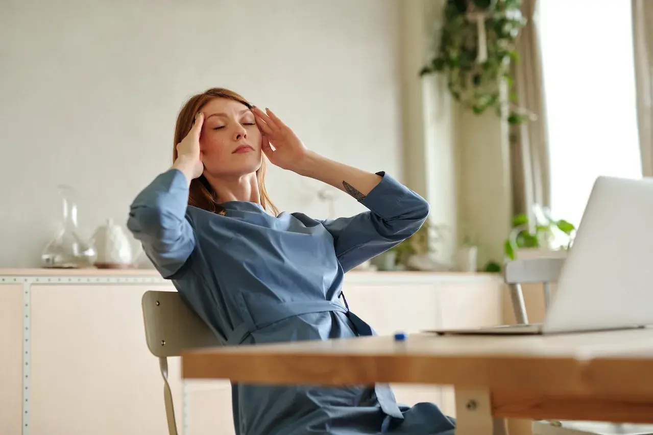 Mujer con dolor de cabeza lado izquierdo, se masajea las sienes con los ojos cerrados.