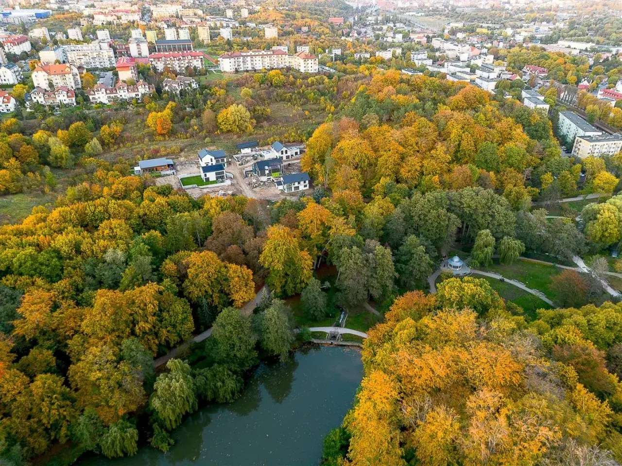 Jesienny widok na park Oruński w Gdańsku. Złote liście drzew otaczają staw, a w oddali widać zabudowania.
