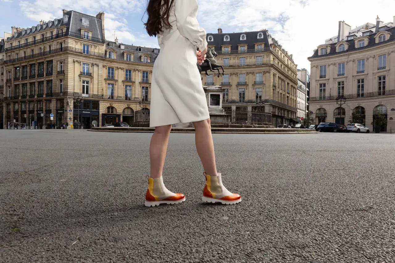 Une femme porte des bottines colorées en plein été, marchant sur une place parisienne.