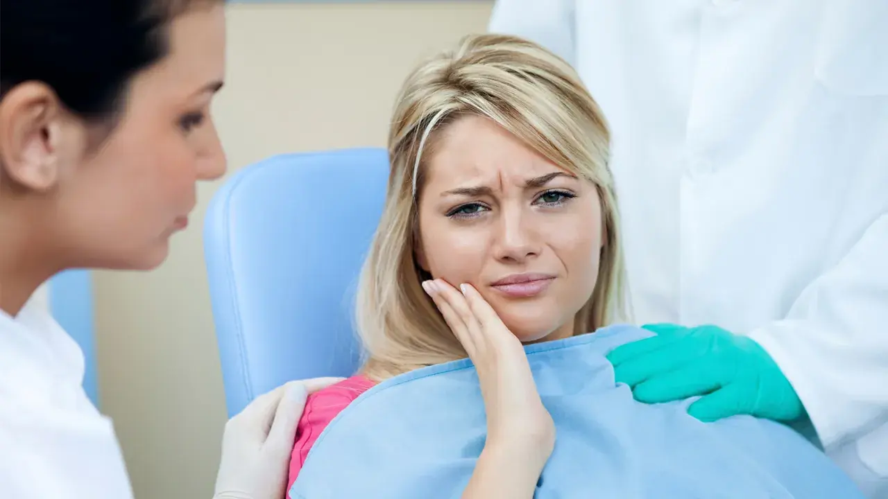 Kobieta cierpi na ból zęba po zatruciu. Dentysta i asystentka próbują jej pomóc.