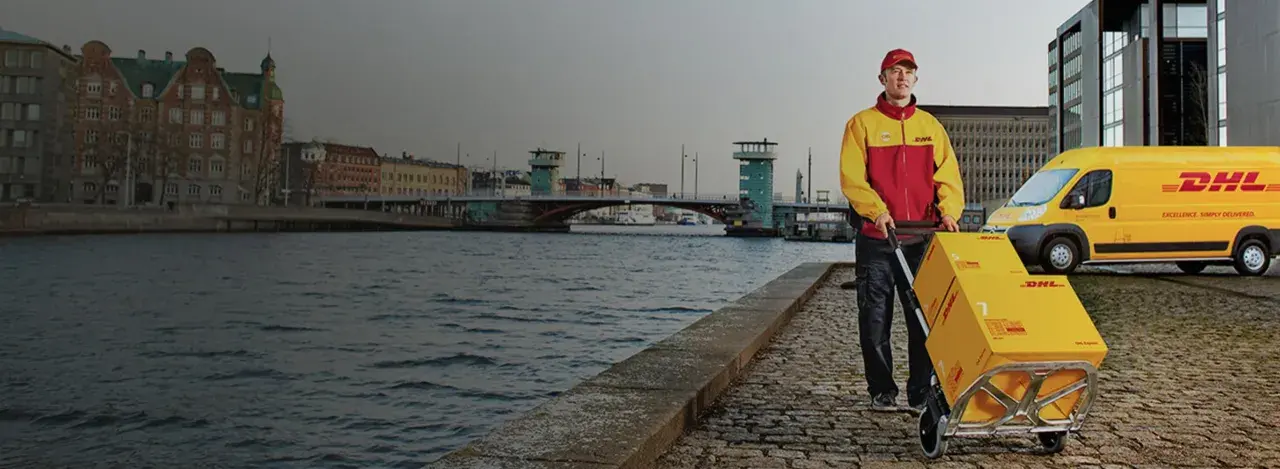 Kurier DHL z wózkiem pełnym paczek obok żółtego vana. Czy u kuriera DHL można płacić kartą? Tak, często jest to możliwe.
