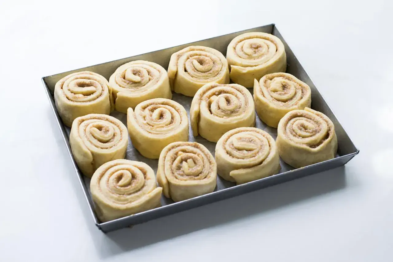 Rotolini alla cannella e mela pronti per essere infornati, disposti in una teglia.