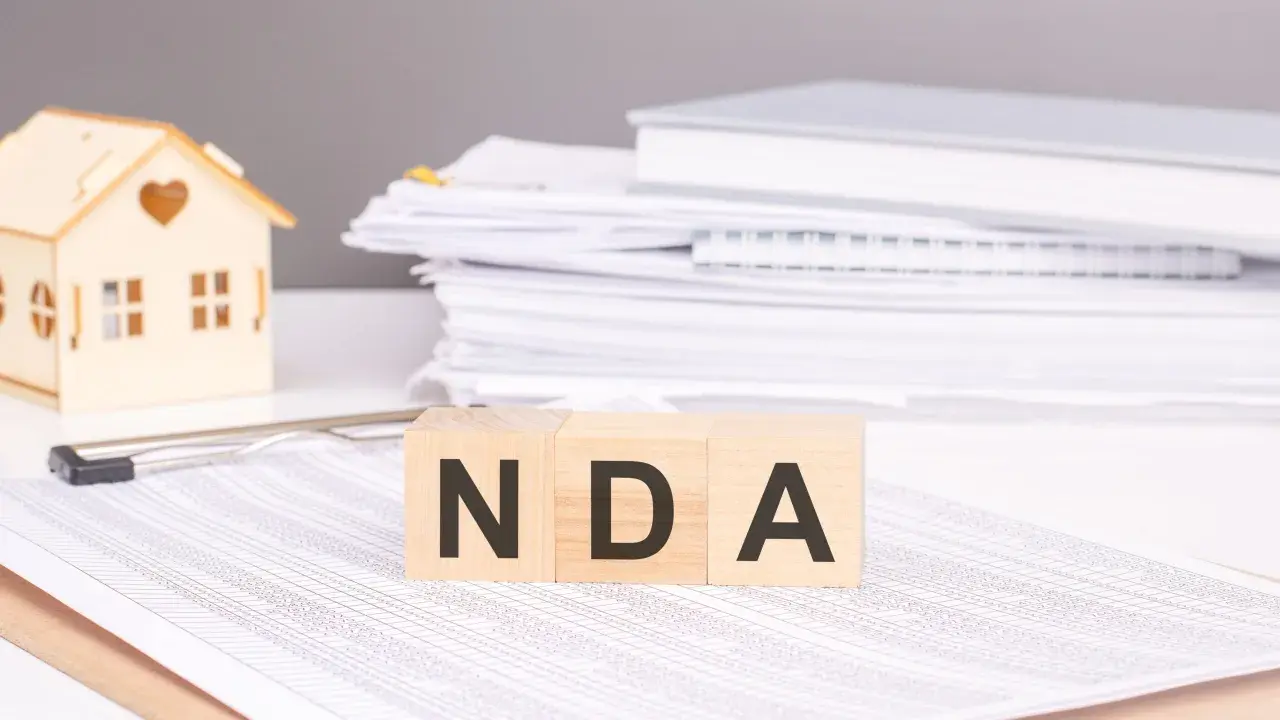 Cubos de madera con las letras NDA, una casa de juguete y pilas de documentos.
