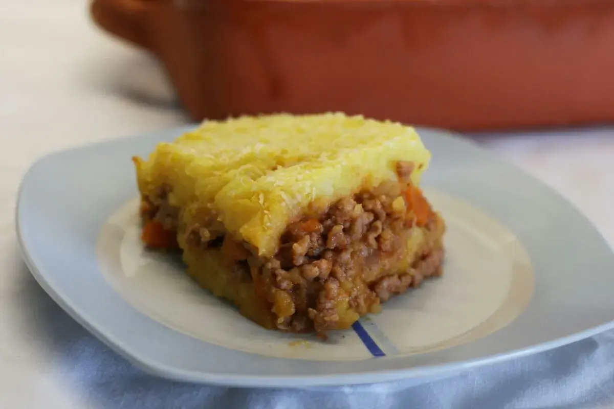 Un trozo de pastel de carne tradicional con puré de patatas gratinado, servido en un plato azul claro.