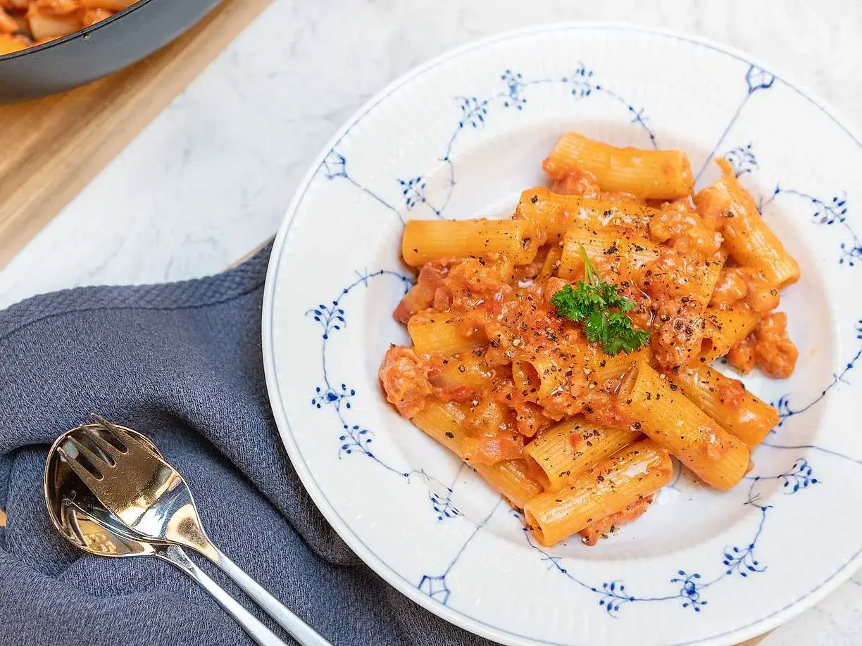 En tallrik med krämig pasta alla zozzona, toppad med persilja och svartpeppar. Bredvid ligger en servett och bestick.