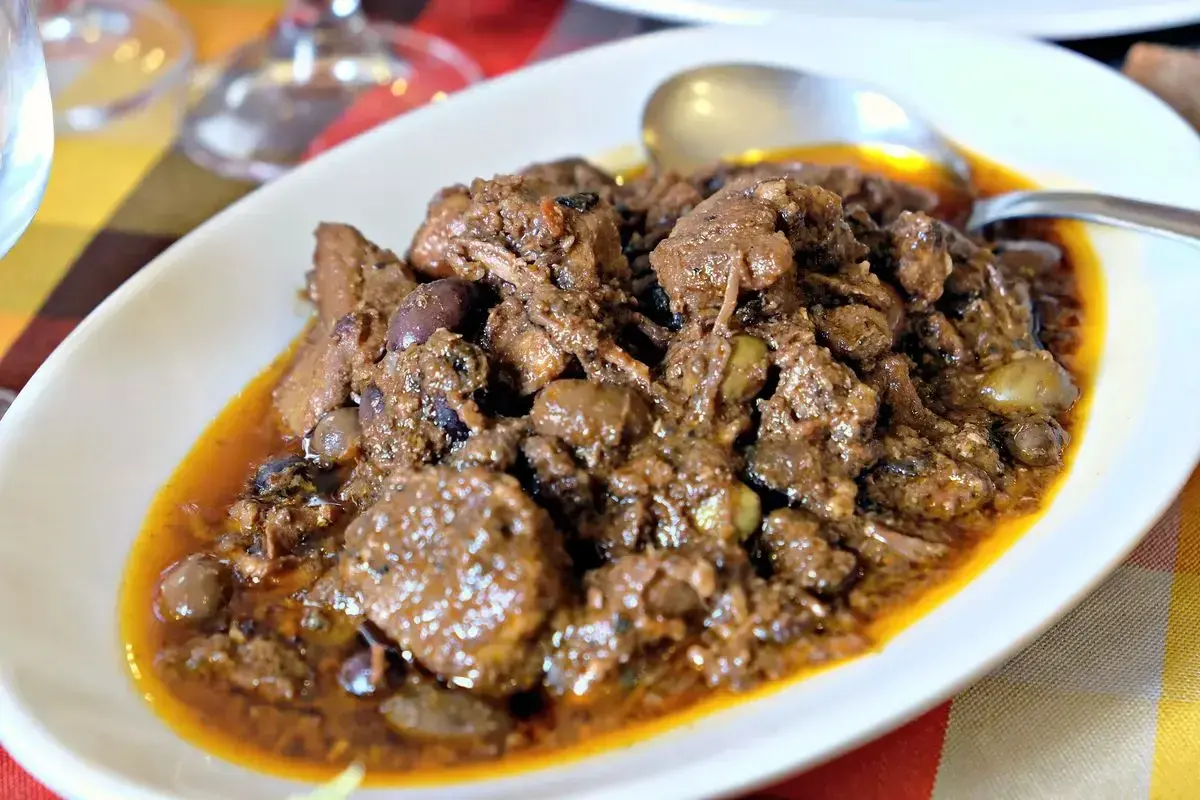 Un saporito cinghiale alla cacciatora, con olive e una ricca salsa, servito in un piatto bianco.