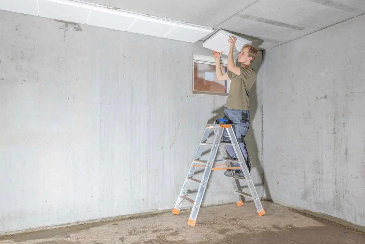 Mann montiert weiße Platten an der Kellerdecke zur Isolierung.